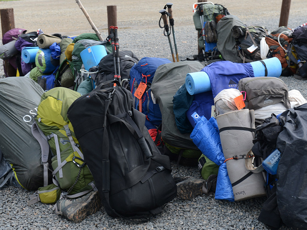 Several backpacks full of hiking gear lined up in rows outside